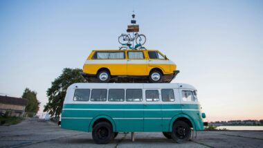 Creative outdoor sculpture featuring a van stacked on a bus with a bicycle on top.